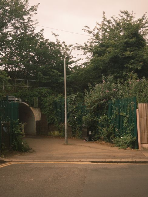The entrance to Hanwell Station is framed by a brick archway, leading into a corridor with a tiled pavement. On either side of the archway, there are black and white signs reading 'HANWELL STATION.' A